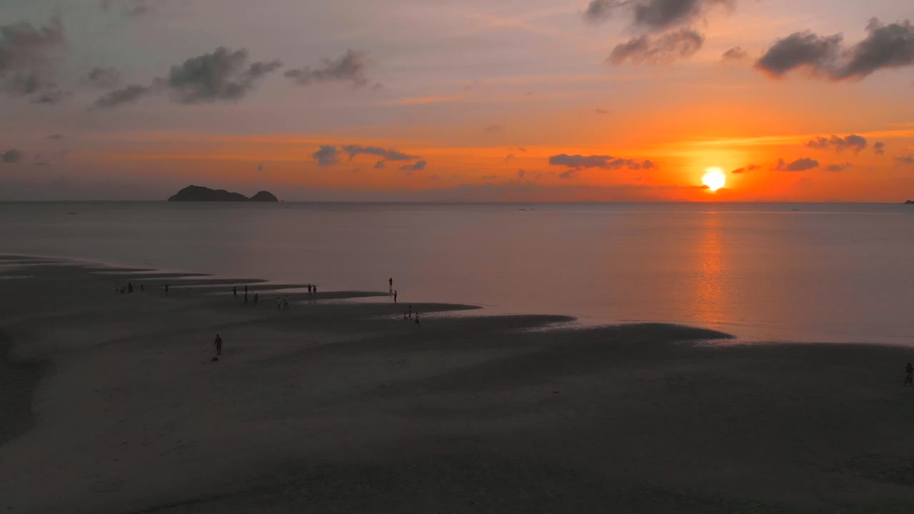 vuelo aéreo sobre la gente que camina en el arrecife de arena en el mar contra la colorida puesta de sol