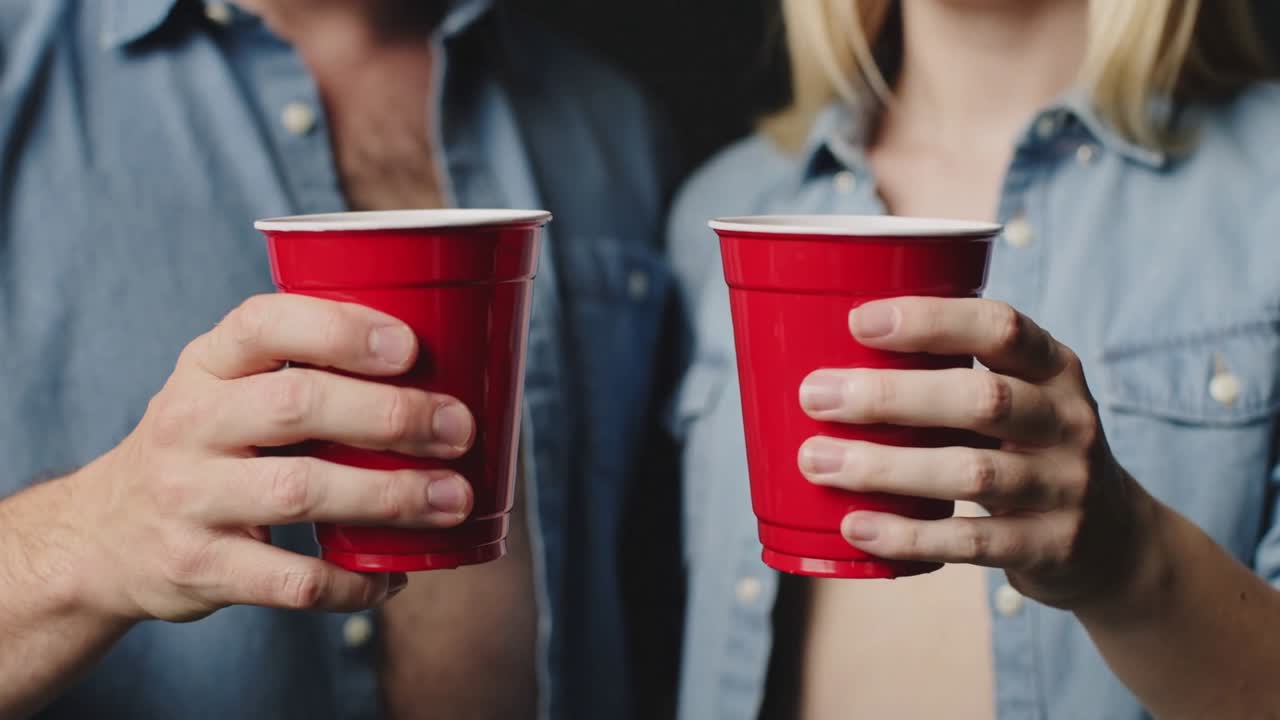 Bringing two red cups together on cue, couple steadying hands in studio with open denim shirts