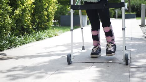 una persona con un yeso en la pierna camina con un caminante en una acera