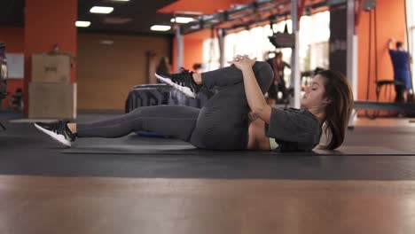 side view of a lying on back woman performs exercise of twisting the body for flexibility. close-up of a female person in a grey elastic sportswear makes gymnastics on floor, stretching her legs