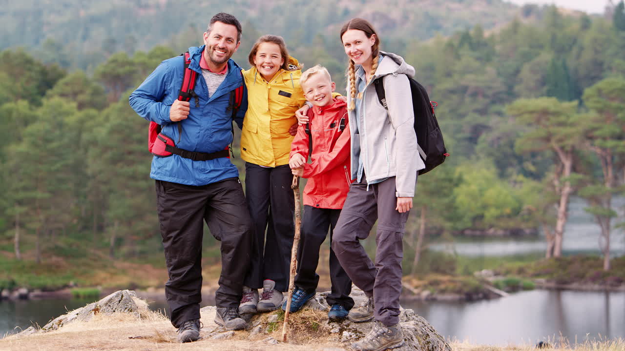 Young family standing on a rock by a lake in the countryside looking to camera laughing, Lake District, UK