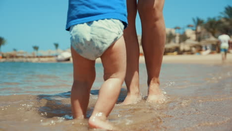 mother and toddler barefoot legs splashing seawater at summer coastline.