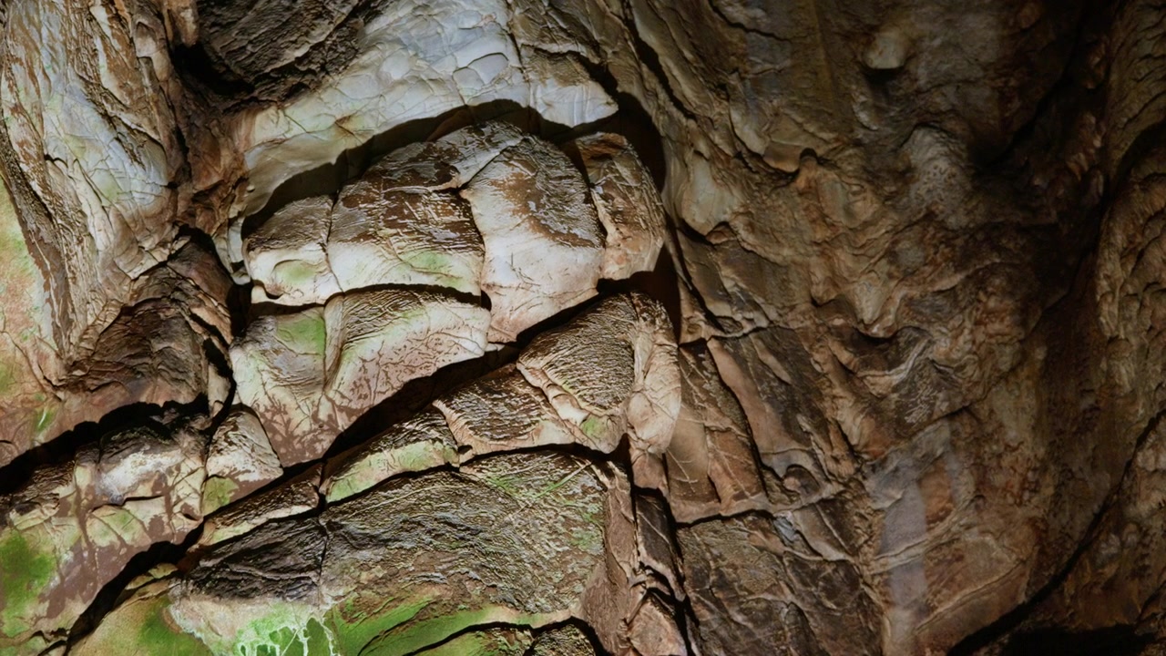 Layered limestone rock formations display textured surfaces with natural mineral deposits inside an underground cave. Static close-up shot captures geological detail with subtle ambient lighting.