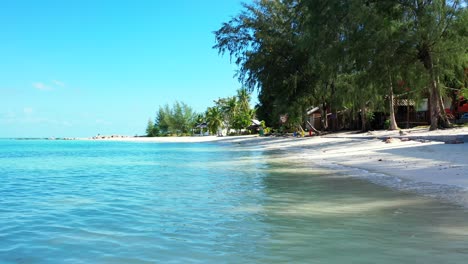 Vibrant-water-of-shallow-lagoon-reflecting-bright-blue-sky-on-shoreline-of-tropical-island-with-white-sandy-exotic-beach-in-Myanmar