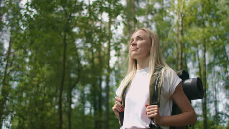 handheld shot of thoughtful serious female hiker with backpack walking amidst trees in forest. a young woman with a backpack walks through the forest on a summer day.