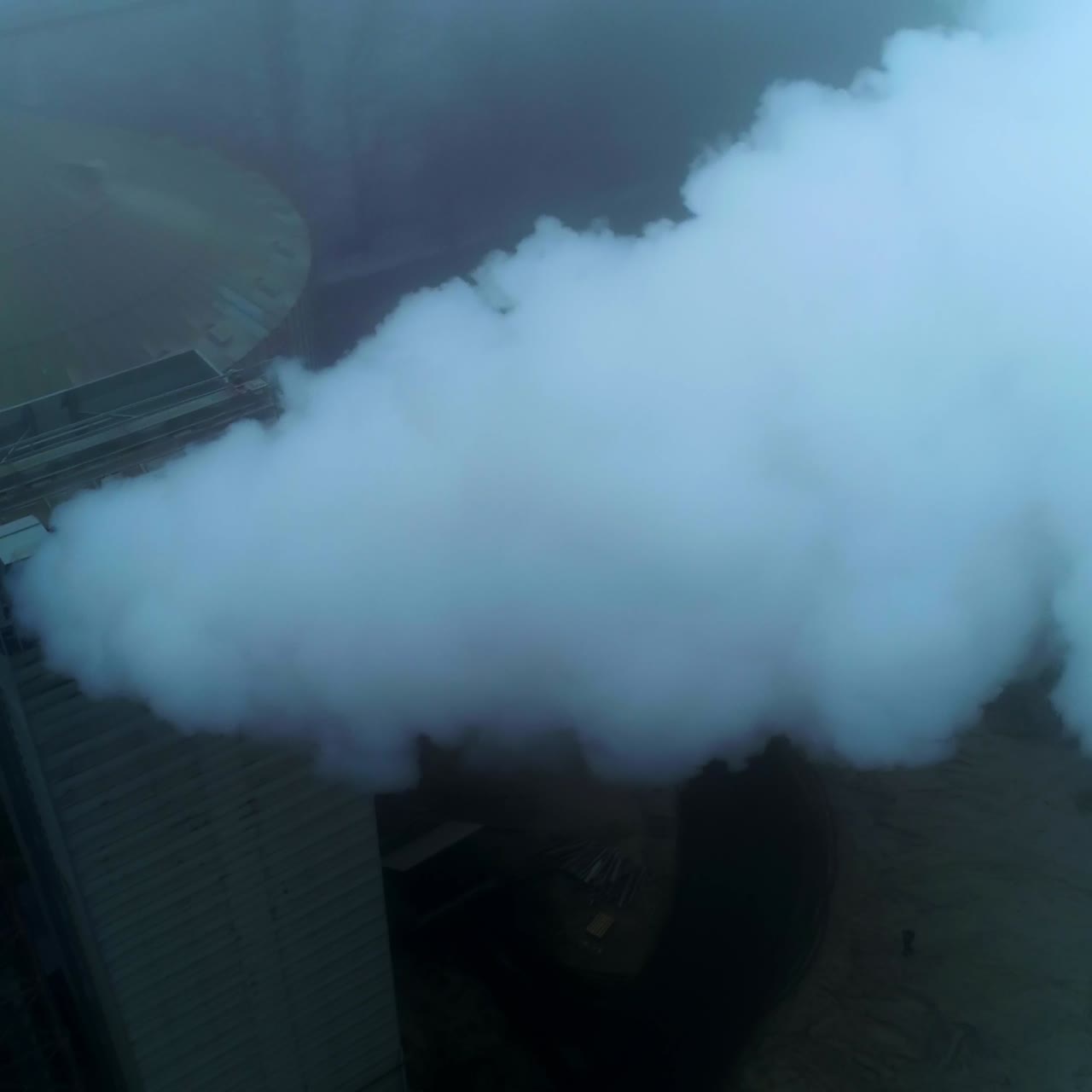 High premises on the territory of grain elevator plant with pipes producing thick smoke. Grey foggy day backdrop