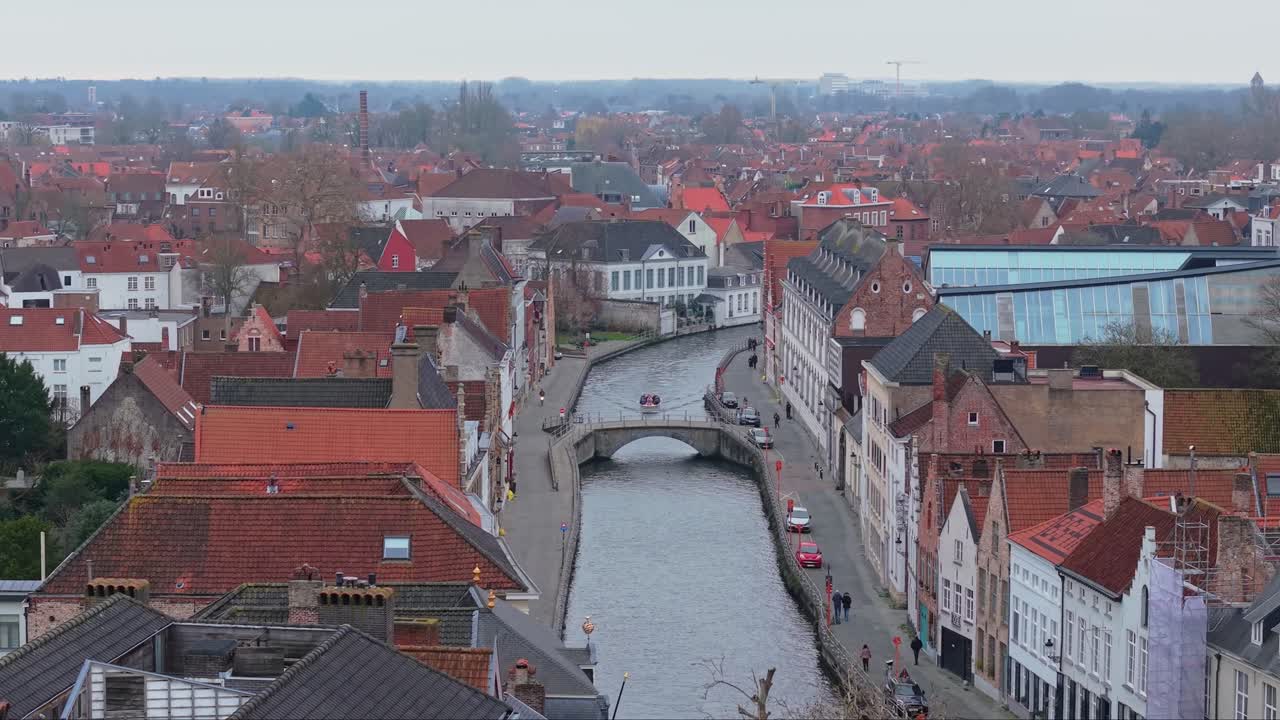 Záběry z dronu historických kanálů v Bruggách v Belgii během ponurého zimního dne. Zatažená obloha se odráží na vodě, obklopené tradiční flámskou architekturou a starobylými cihlovými domy