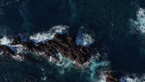 volcanic rocks in beautiful sunny turqouise ocean with waves crashing onto them creating sea foam