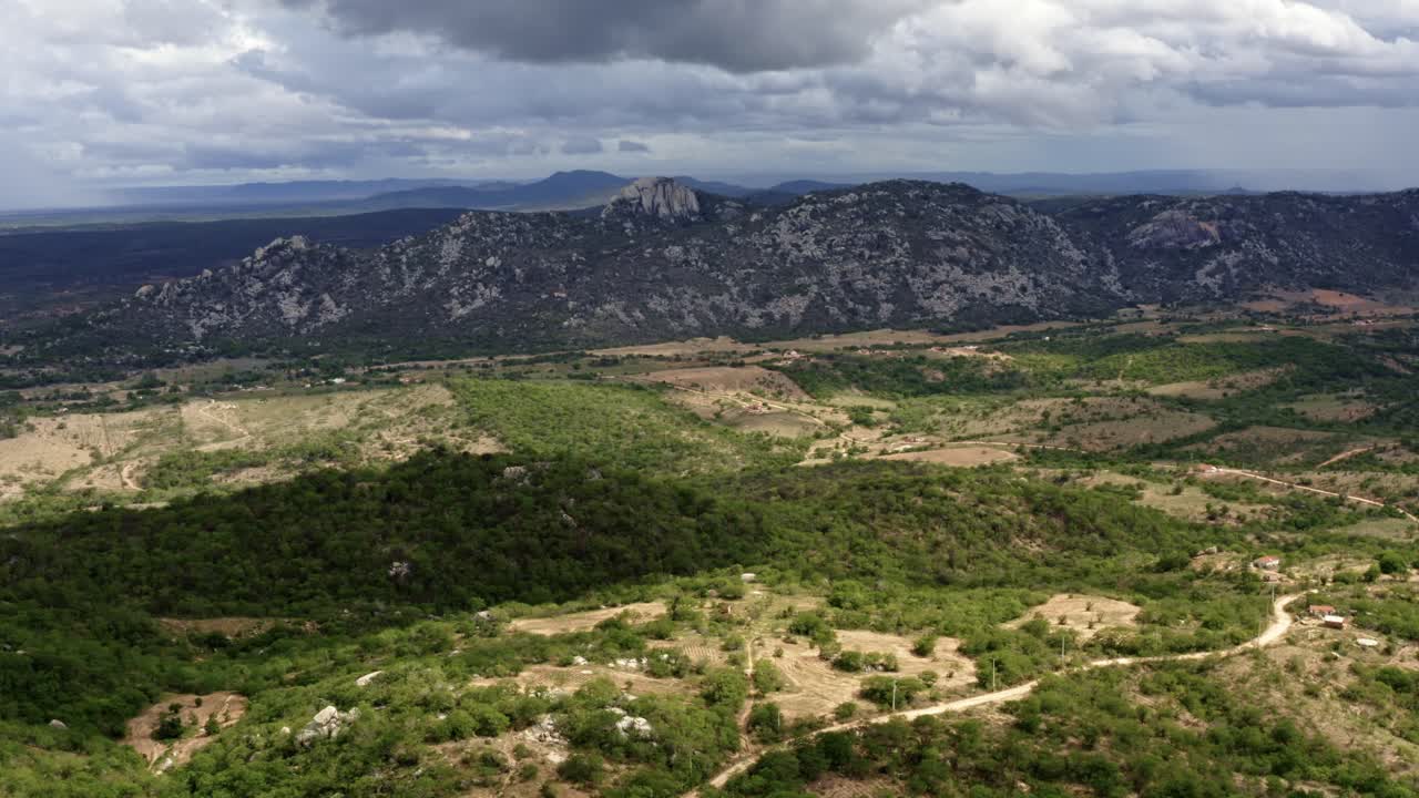 Tilting up aerial drone extreme wide shot of the mountain range of the Pedra de Sao Pedro in Sítio Novo, Brazil in the state of Rio Grande do Norte in the countryside with rural homes and farmland