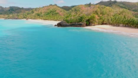 Drone-flight-over-blue-Caribbean-Sea-along-Playa-Breman-Beach-and-scenic-landscape-in-background