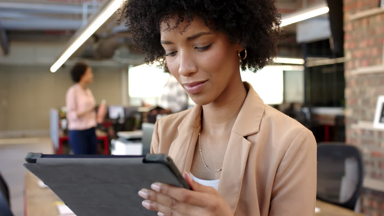 Biracial woman using tablet in modern office, open workspace with colleagues working
