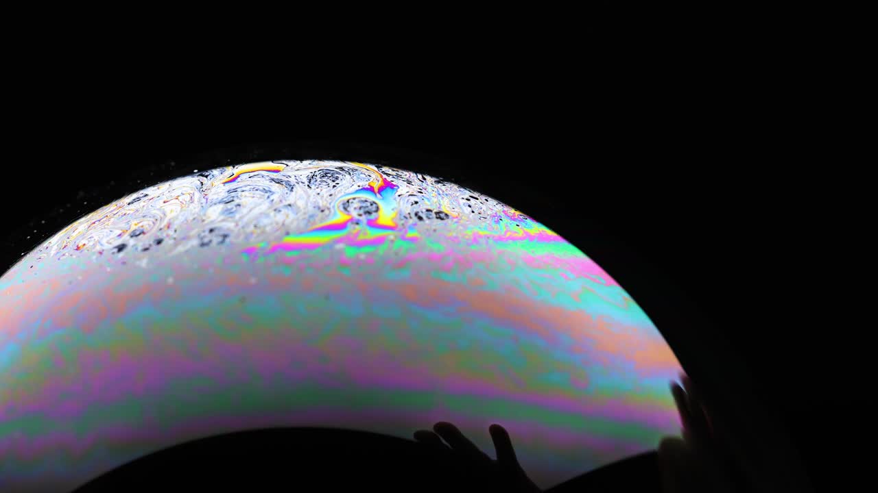 Vibrant soap bubble displays shifting colors and reflections against a dark background, capturing dynamic light and texture changes