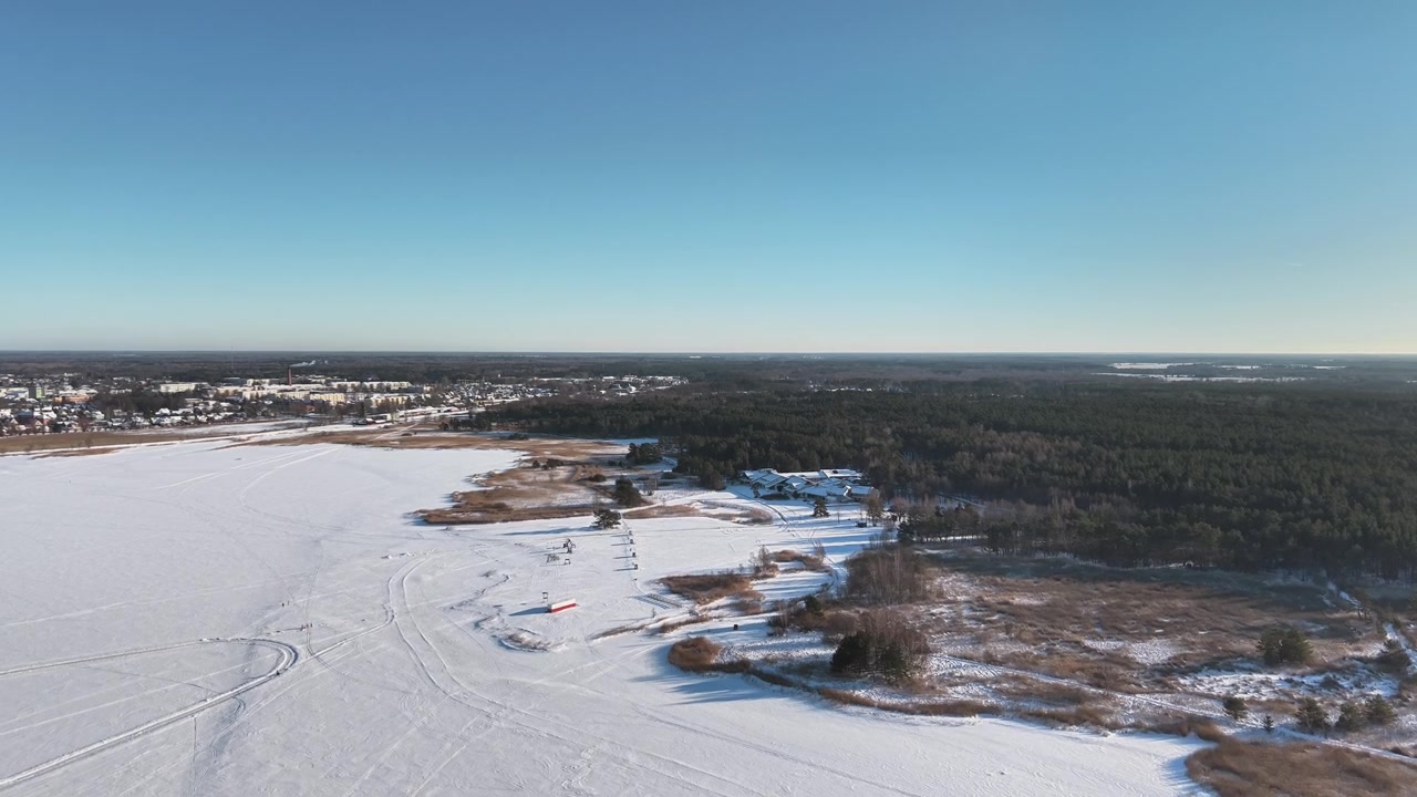 Dronen ilmakuva jäätyneestä rannikosta ja lumisesta maisemasta Haapsalun, Viron, lähistöllä, jossa näkyy jäinen meri ja talvimaisema kirkkaan sinisen taivaan alla.