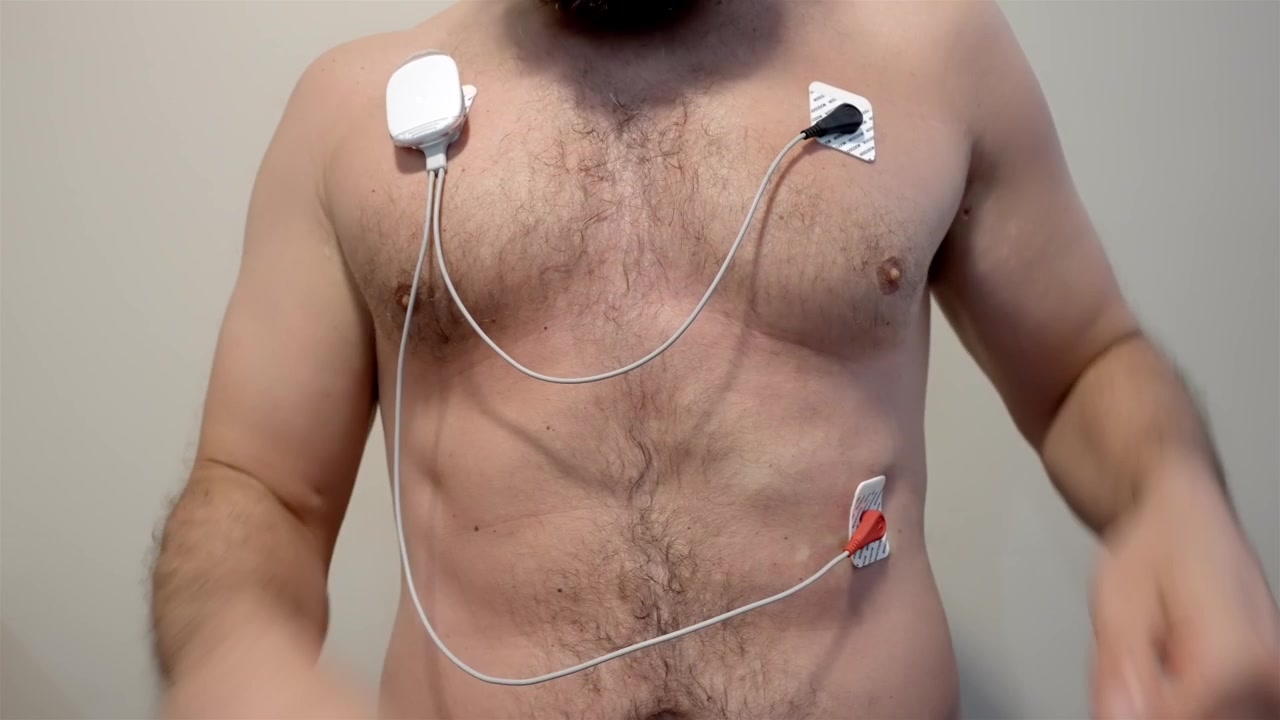 Uomo a torso nudo sistema un monitor cardiaco portatile contro una semplice parete interna