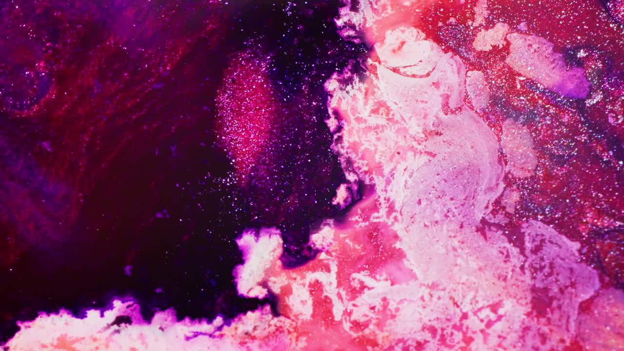 Macro view of violet ink added to shimmering red and pink ink, with intense fluid motion, swirling patterns and sparkling textures