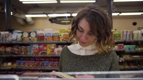 young curly haired woman doing grocery shopping at the supermarket, she is reading a product label and nutrition facts on a box