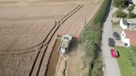 aerial footage of a combine harvester harvesting a wheat crop next to homes