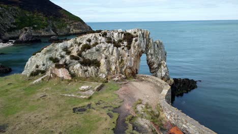 Aerial-view-circling-scenic-rock-archway-on-the-Welsh-coastline-with-calm-blue-ocean