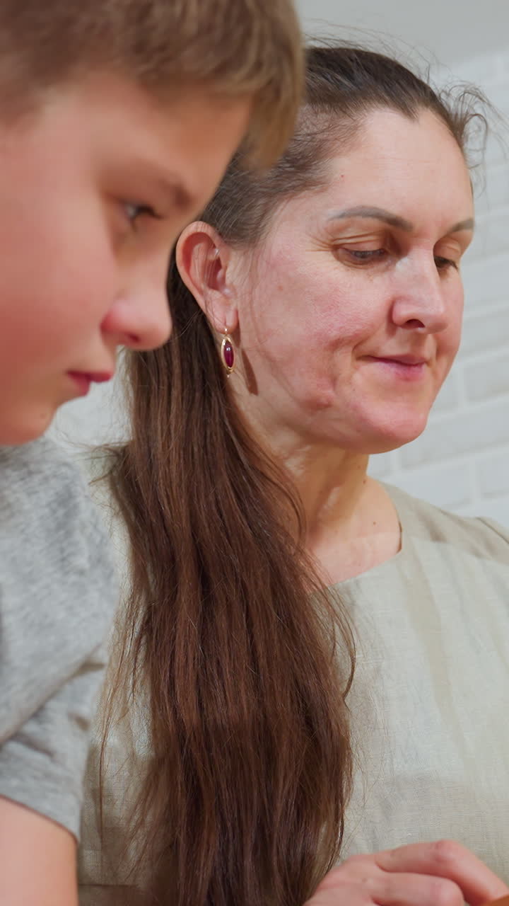 환한 실내 조명 아래, 코카서스인 엄마와 아들이 책을 읽는 클로즈업 사진이에요. 엄마는 인내심 있는 표정으로 아이에게 몸을 기울이고, 아이는 집중하고 있어요. 조용한 집 서재에서 따뜻한 교감을 나누며 엄마가 아이를 가르치는 모습, 부드러운 얼굴 표정이 인상적이네요.