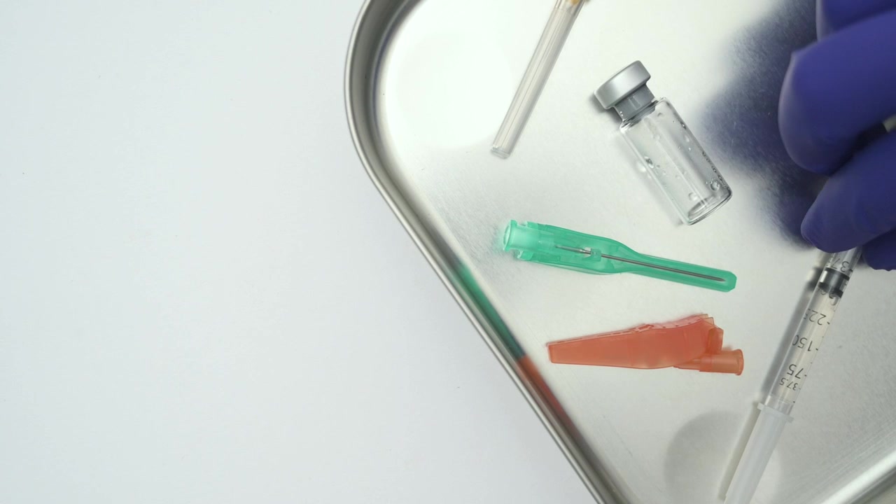 Medical professional arranging vaccination supplies on a steel tray against a white background