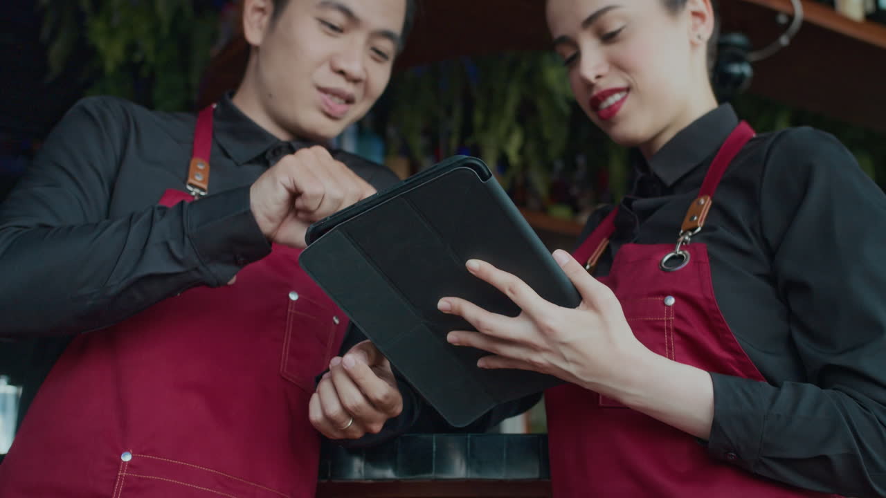 Waitress Explaining New Waiter How to Use App on Tablet in Cafe