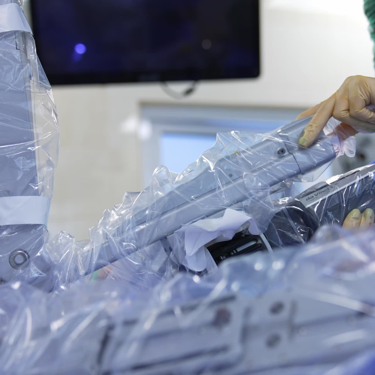 Switched on Da Vinci robot working in the surgery room. Advanced equipment covered in plastic is moved by the hands of medic in latex gloves