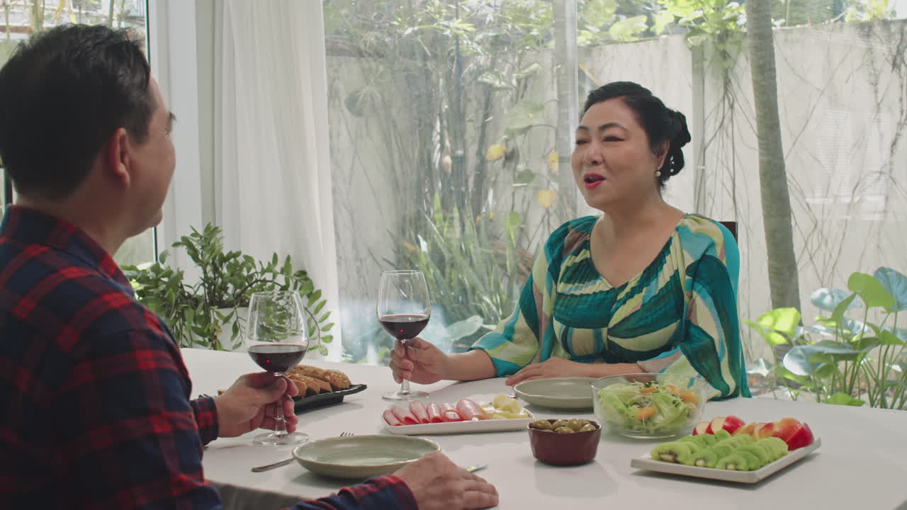 Aged Spouses Drinking Red Wine at Dinner Table with Snacks
