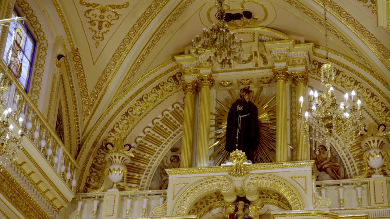 Vista interna di un altare di chiesa ornato con statua religiosa, lampadari e architettura barocca decorativa durante una celebrazione festiva a Cholula, Puebla, Messico.