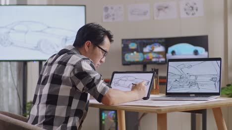 vista lateral de un hombre asiático dibujando un nuevo concepto de diseño de automóvil en una tableta en el estudio con televisión y computadoras muestra modelo de automóvil eléctrico 3d