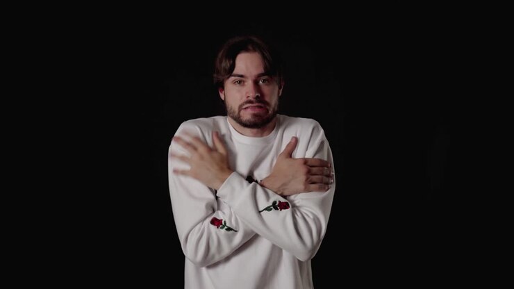 Giovane uomo trendy che mima il freddo, tremando e riscaldandosi, inquadratura ampia, sfondo nero.