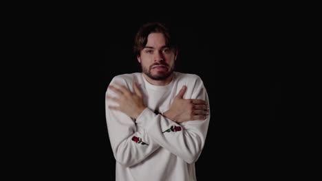 trendy young man freezing gesture, shaking and warming himself, wide, black background