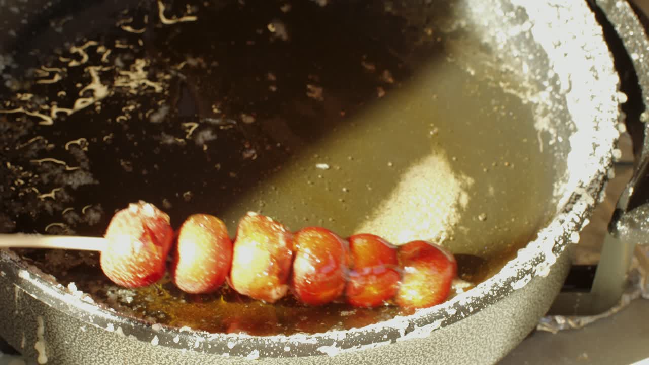 Making fruits in boiling caramel close-up. Chinese winter sweet dessert Tanghulu street food.Berries, grapes, tangerine and others fruit caramelized in sugar. Asian street market with traditional food.. High quality 4k footage