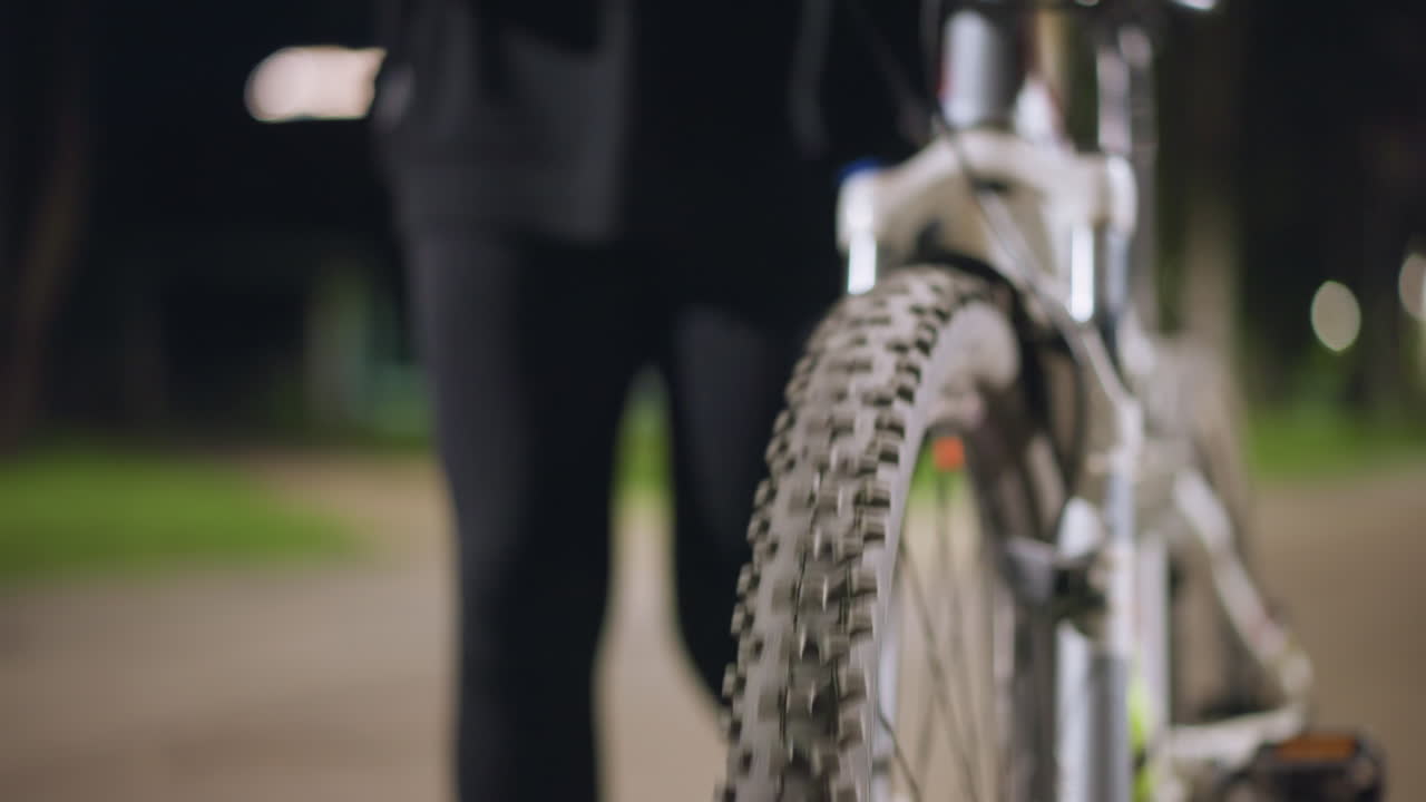 Lonely Cyclist Waiting Quietly, Nighttime Scene Showing Stopped Cyclist, Still Scene Of Cyclist Halted On Quiet Street, Calm Nighttime Street Scene Featuring Front Wheel Closeup And Resting Legs