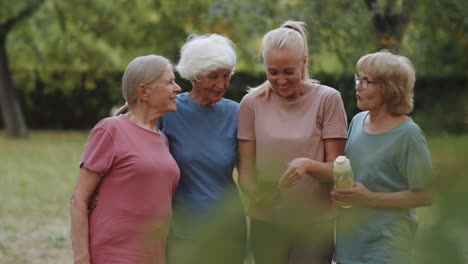 senior women and female trainer chatting and using smartphone outdoors