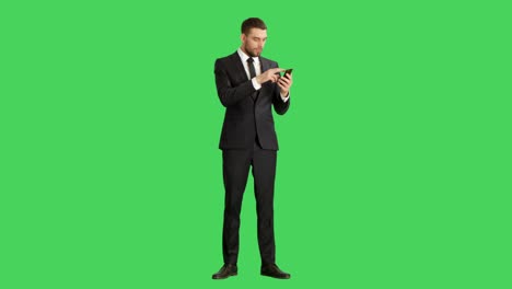long shot of a handsome businessman holding smartphone with one hand and making swiping touching gestures with another. tablet and background are green screen.
