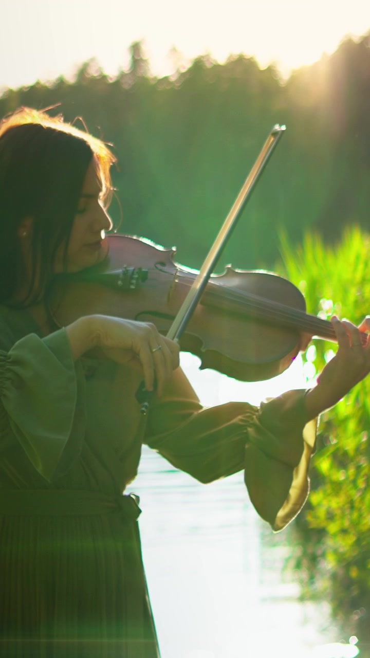 Woman Playing Violin Outdoors at Sunset by a Lake