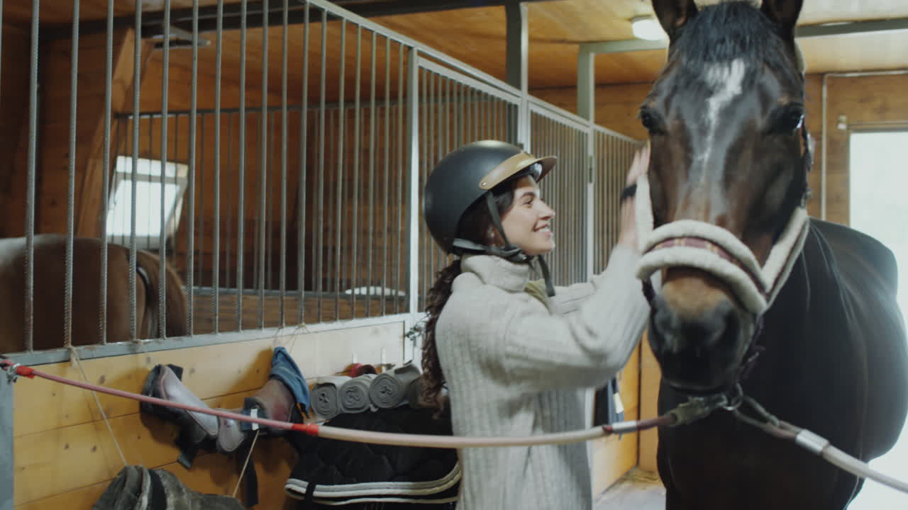 Woman in a riding helmet interacting with a horse in a stable