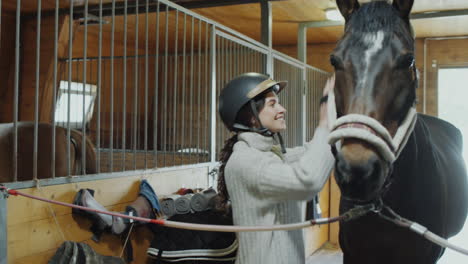 woman in a riding helmet interacting with a horse in a stable