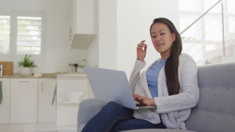 Happy-asian-woman-sitting-on-sofa,-resting-with-laptop-at-home