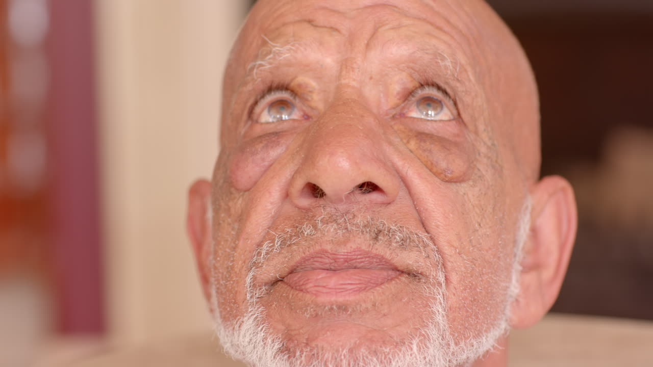 Elderly man with thoughtful expression looking away, reflecting on memories, at home