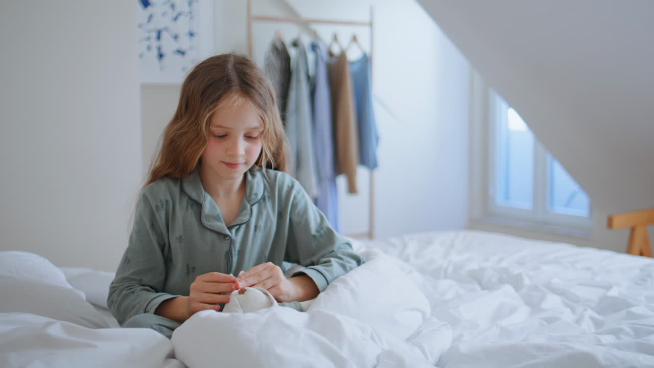 Child holding plush bunny at bedroom closeup. Carefree little girl in pyjamas