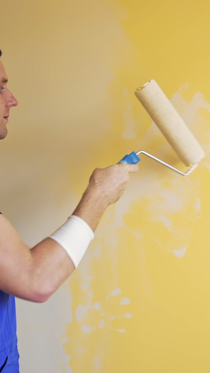 Young worker painting wall in room. Repair, building and home concept. Vertical video