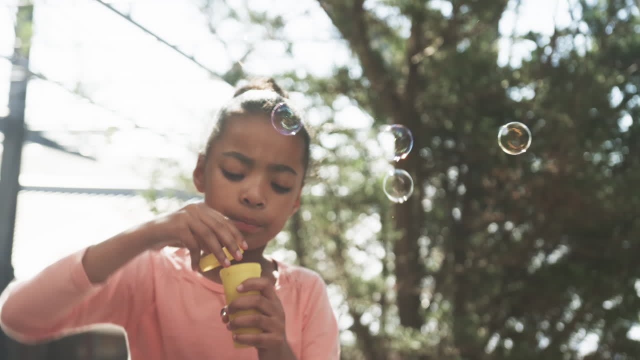 Blowing bubbles, young African American girl enjoying outdoor activity at school playground