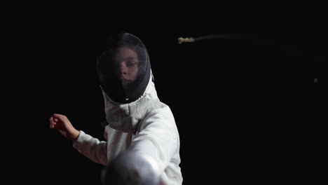 a young woman fencer in white uniform with a mask and foil in hand. she is in action during a fencing competition. the background is black and the image is blurred due to motion.