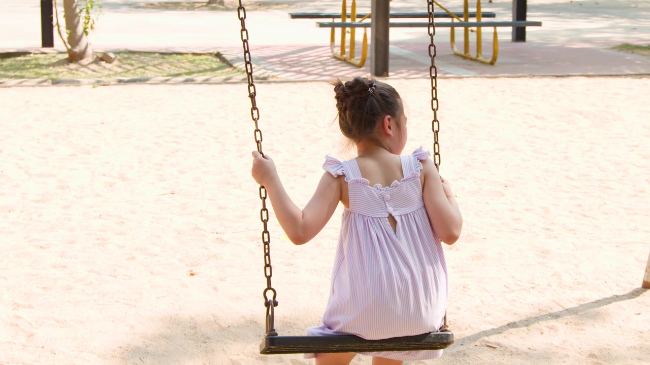 Una giovane ragazza si dondola su un parco giochi al Parco Lumpini, Bangkok, durante una giornata di sole