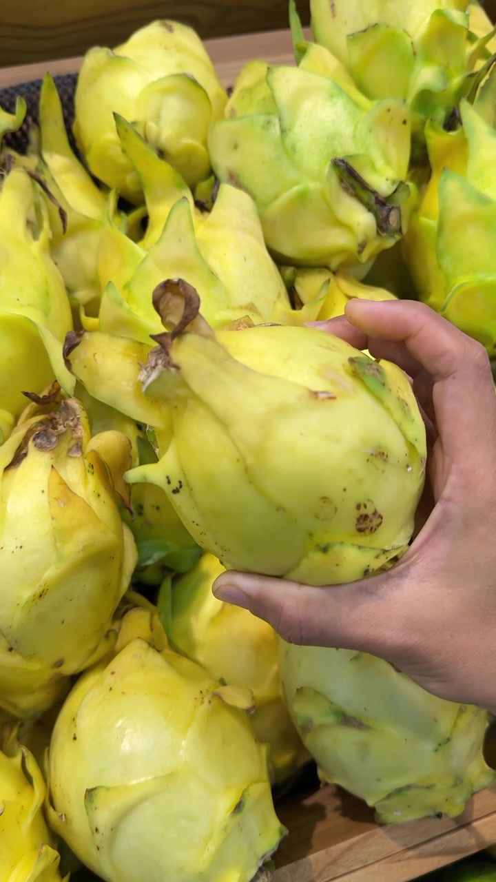 Mano che seleziona un frutto del drago giallo fresco al supermercato