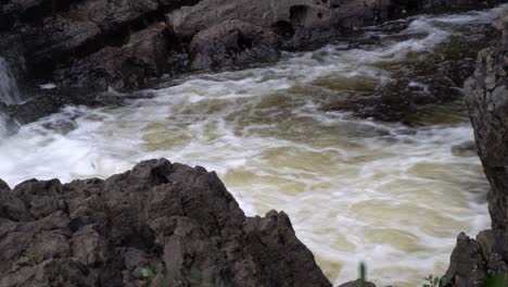 Agua-Que-Fluye-Sobre-Rocas-Y-Espuma-Batida-Bajo-Una-Cascada