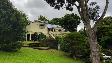 Smooth-slow-cinematic-shot-of-the-back-of-a-classic-traditional-country-Queenslander-house,-with-a-splendid-back-deck,-nestling-in-neatly-manicured-landscaped-garden,-under-cloudy-skies