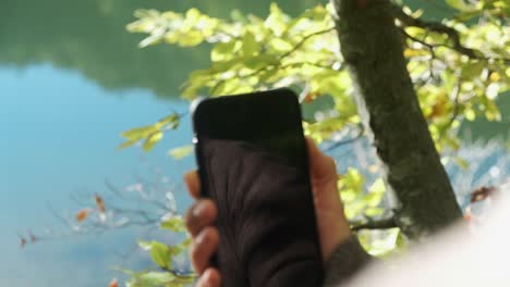 woman's finger turn off cellphone in forest with calm lake in background