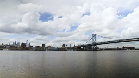 Skyline-Von-Philadelphia-über-Dem-Ruhigen-Delaware-River-Mit-Der-Benjamin-Franklin-Brücke-An-Einem-Wolkigen,-Warmen-Tag